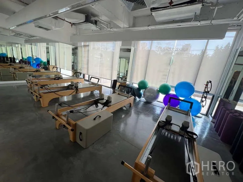 Retail Space for rent - Sunlit studio room with floor-to-ceiling windows, Pilates reformer machines, and exercise balls.