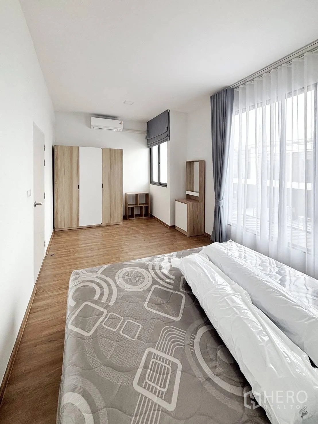 Townhouse for rent in Bang Phli, Samut Prakan - Spacious master bedroom with large window, sheer curtains, wood flooring, wardrobe and air conditioner.
