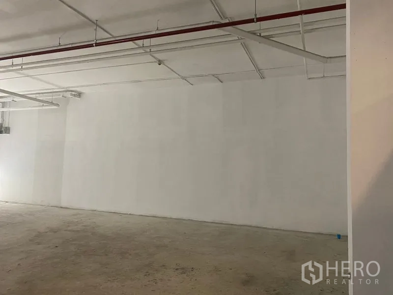 Retail Space for rent - Expansive unit wall with exposed sprinkler and piping across the white ceiling.