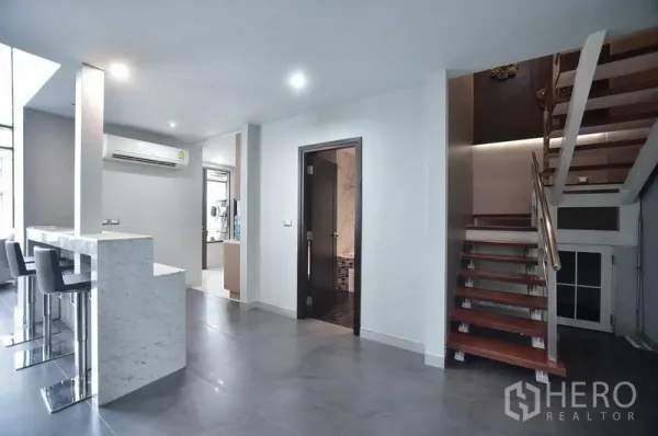 Condominium for rent in Khlong Toei, Bangkok - Marble breakfast bar with bar stools beside a hallway and wooden staircase leading to the upper level.