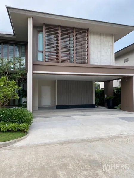 Detached House for sale in Bang Kapi, Bangkok - Covered double carport beneath a cantilevered second floor with wood slat screens and neat hedges.