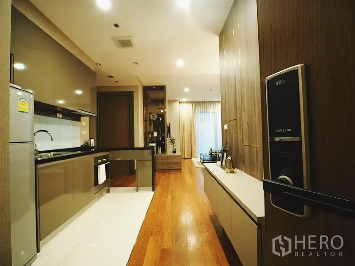 Condominium for rent in Khlong Toei, Bangkok - Entry view to sleek galley kitchen and wood-floored living area with smart door lock.