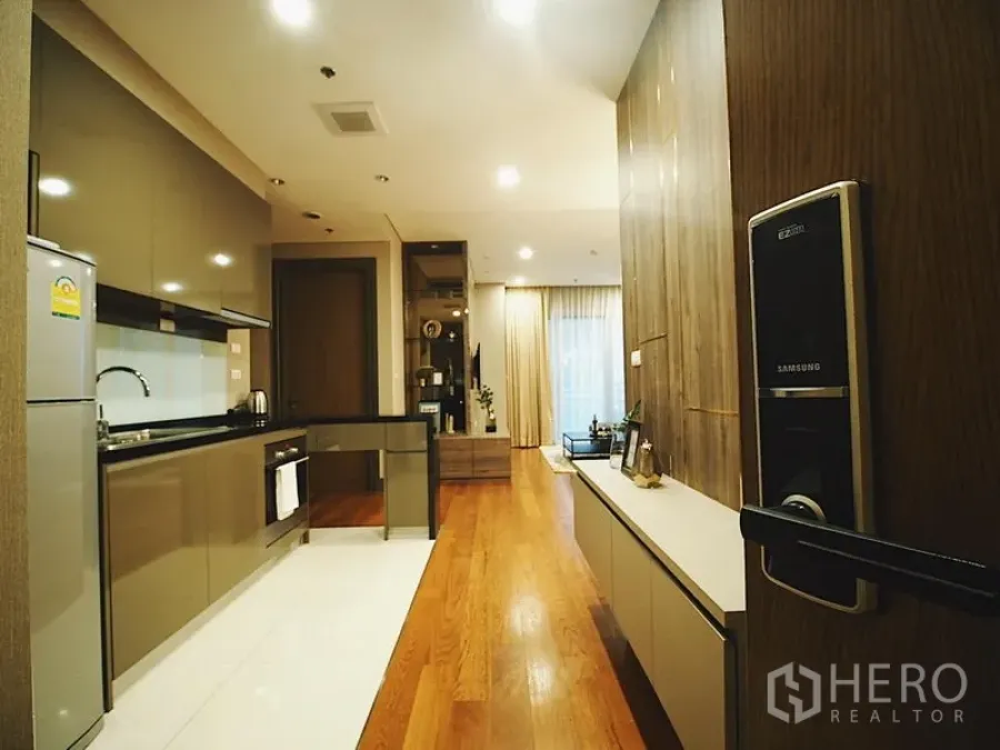 Condominium for rent in Khlong Toei, Bangkok - Entry view to sleek galley kitchen and wood-floored living area with smart door lock.