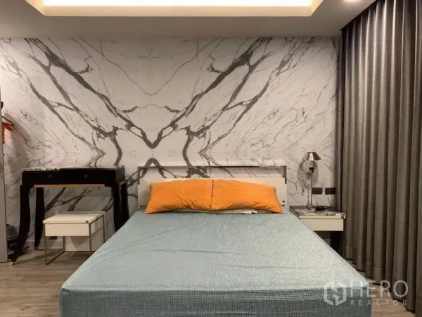 Condominium for sale in Khlong Toei, Bangkok - Bedroom featuring a dramatic marble-pattern wall, upholstered bed with orange pillows, bedside tables and blackout curtains.