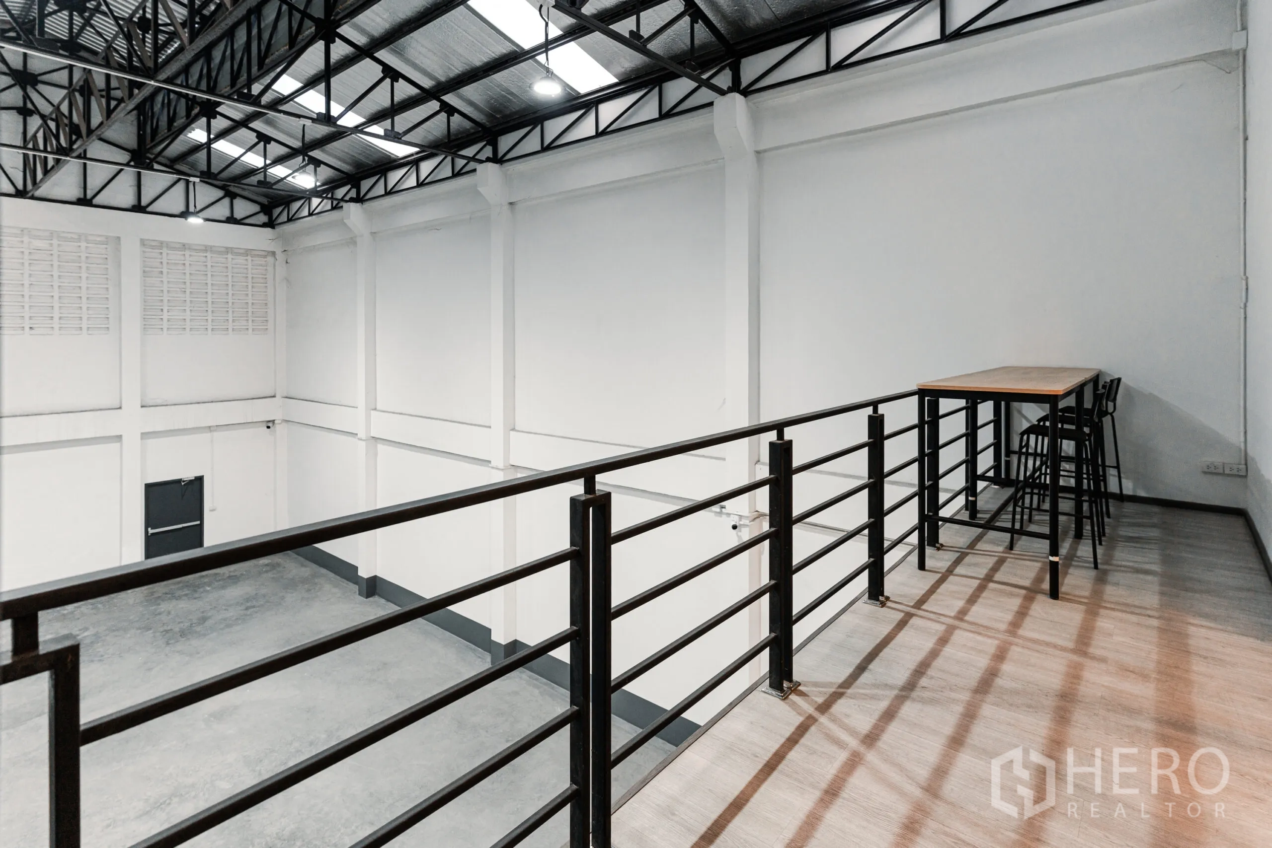 Warehouse for rent in Mueang Samut Sakhon, Samut Sakhon - Mezzanine railing viewpoint overlooking the warehouse floor with bar-height table, chairs and lighting.