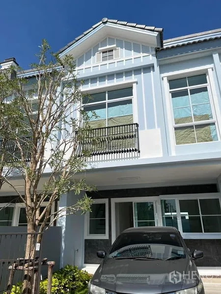 Townhouse for rent in Prawet, Bangkok - Two-storey Indy 2 townhouse facade with balcony, large windows, and driveway parking under a gabled roof.