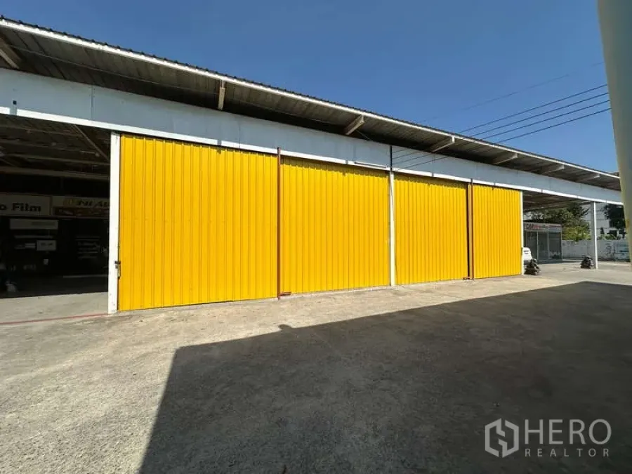 Warehouse for rent in Bang Khen, Bangkok - Yellow sliding steel doors of a warehouse with a wide concrete loading yard in Bang Khen.