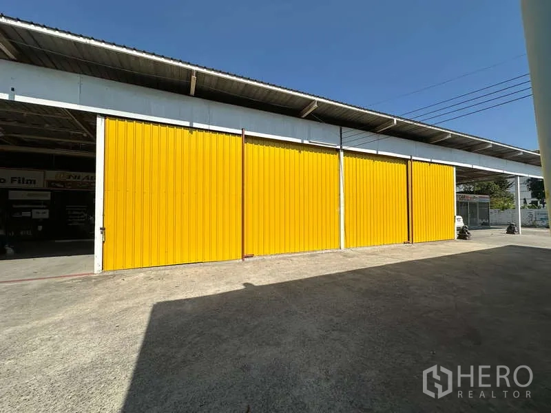 Warehouse for rent in Bang Khen, Bangkok - Yellow sliding steel doors of a warehouse with a wide concrete loading yard in Bang Khen.