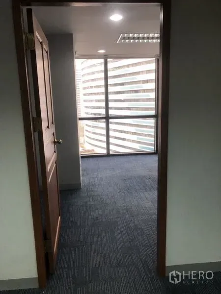 Office Space for rent - Hallway leading to a windowed office room with city views and blue carpet flooring.