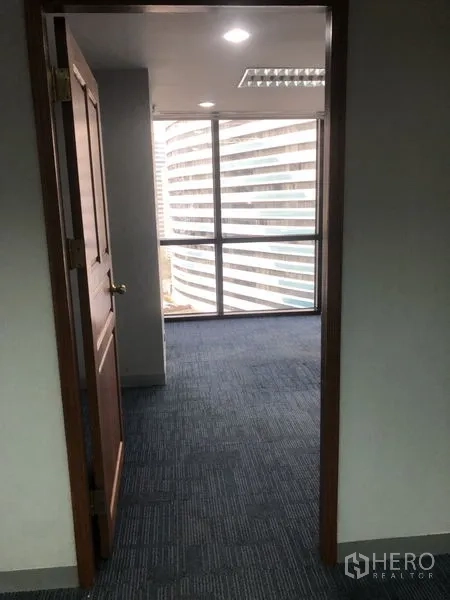 Office Space for rent - Hallway leading to a windowed office room with city views and blue carpet flooring.