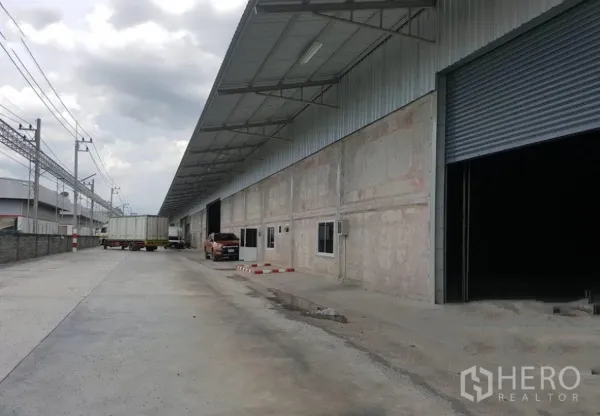 货栈 出租在Lam Luk Ka, Pathum Thani - 装卸区，卡车停靠在雨棚下的仓库旁。