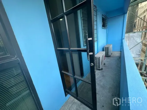 办公空间 出租在Bang Rak, Bangkok - 蓝色外墙的狭长阳台，黑框玻璃门与室外空调机组，可望城市景观。