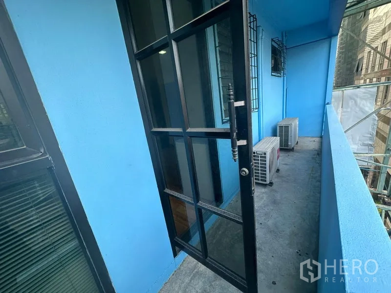 办公空间 出租在Bang Rak, Bangkok - 蓝色外墙的狭长阳台，黑框玻璃门与室外空调机组，可望城市景观。