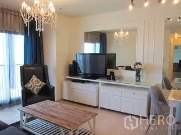 Condominium for rent in Khlong Toei, Bangkok - Bright living room with chandelier, TV console and sliding doors to a balcony.