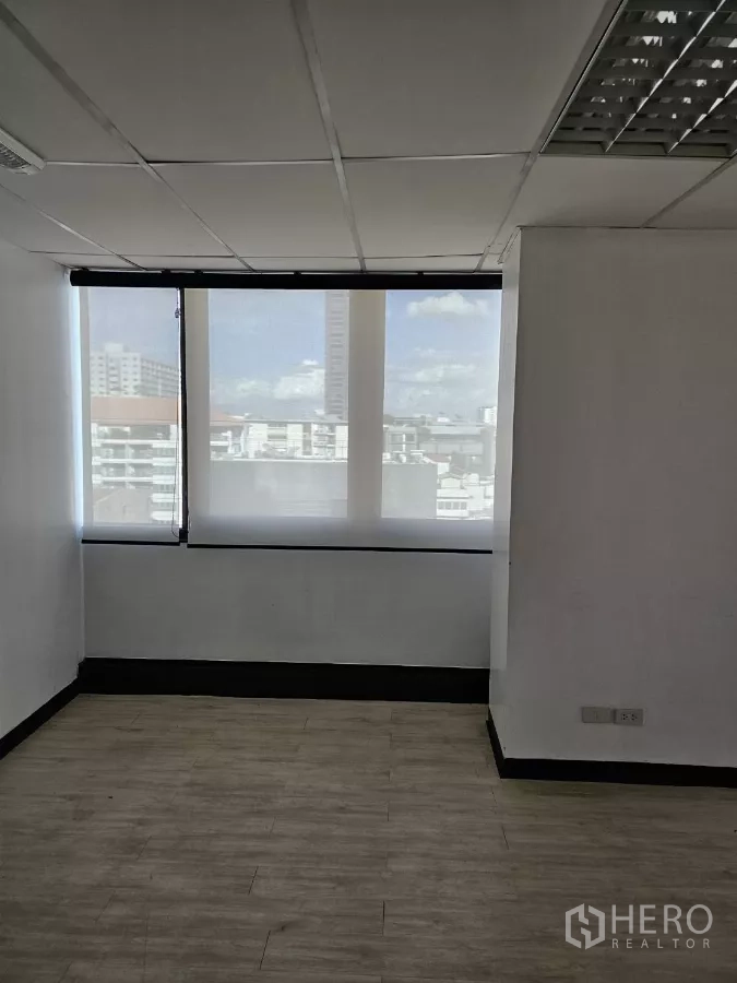 Office Space for rent in Watthana, Bangkok - Compact office room with two tall windows, sheer blinds, and light wood flooring.
