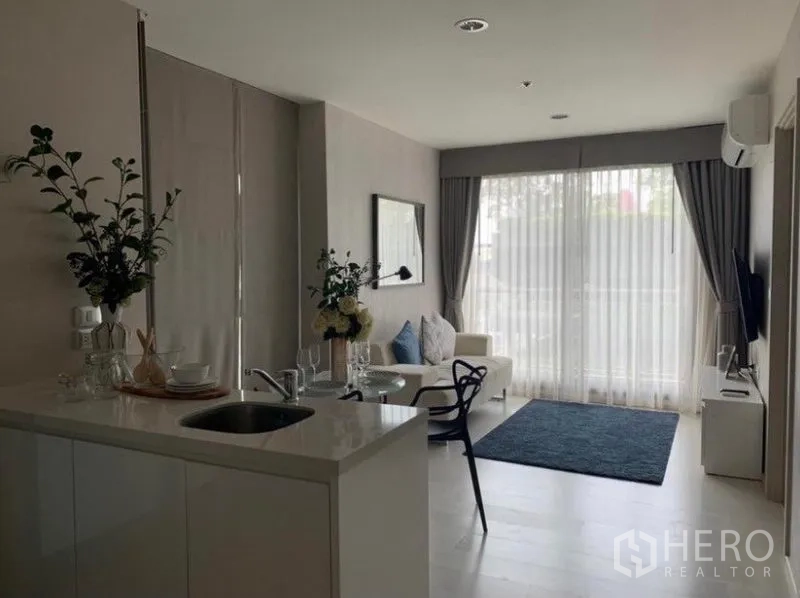 Condominium for rent in Khlong Toei, Bangkok - Open-plan living room with white kitchenette island, sofa, and floor-to-ceiling windows with sheer curtains.