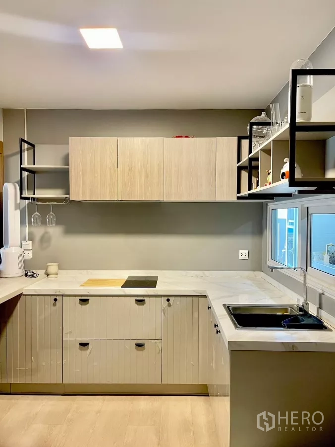 Detached House for rent in Prawet, Bangkok - L-shaped modern kitchen with marble-look counters, sink and cooktop.