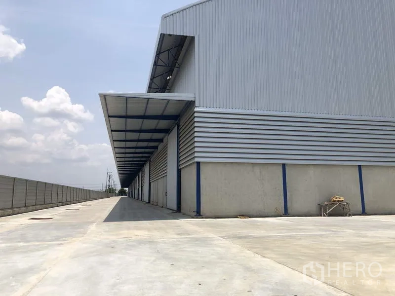 Factory for rent or sale in Lat Lum Kaeo, Pathum Thani - Side elevation of the factory showing a long covered loading bay and wide concrete driveway.