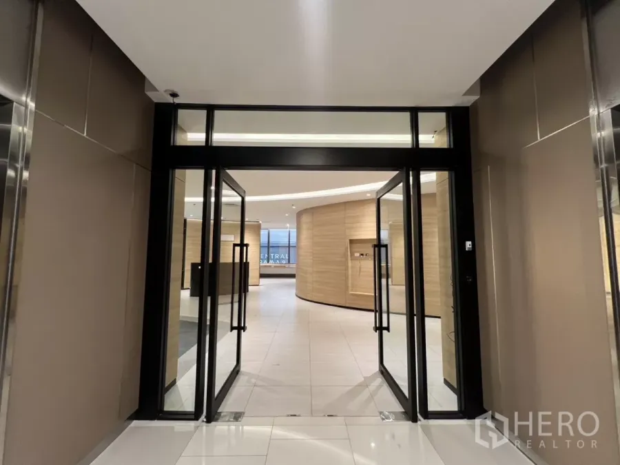 办公空间 出租在Huai Khwang, Bangkok - 玻璃双开门通向现代办公大堂，木纹墙面与白色地砖。