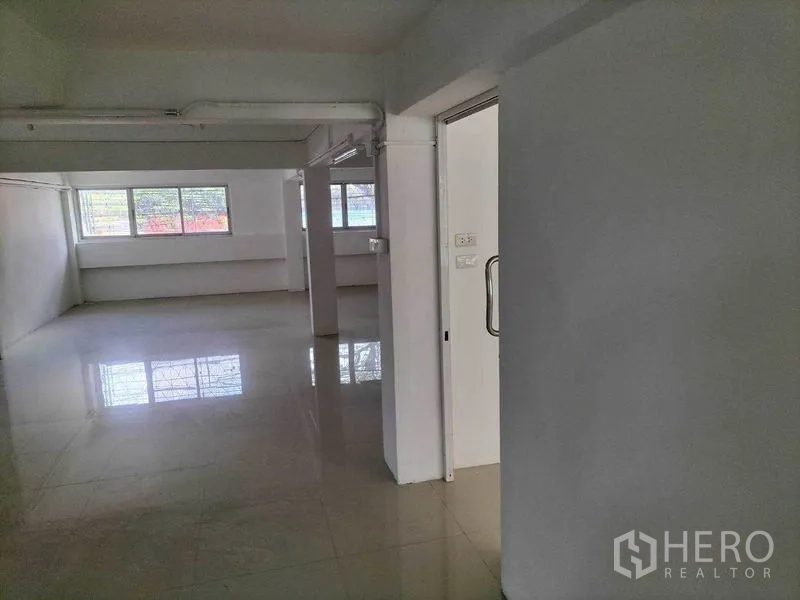 Shophouse for rent in Khlong Toei, Bangkok - Open-plan upper floor with glossy tiles, large windows and a doorway with glass handle.