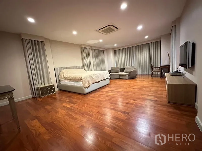 Detached House for rent or sale in Khan Na Yao, Bangkok - Expansive bedroom with bed, sofa set, study desk and wall-mounted TV.