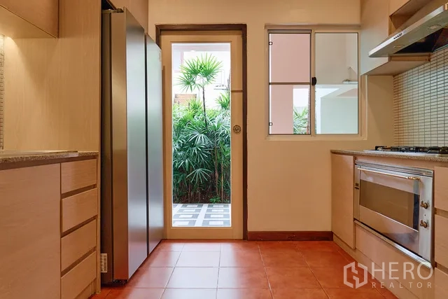 Detached House for rent in Watthana, Bangkok - Kitchen corridor with tall refrigerator, cabinetry and door to a garden courtyard.