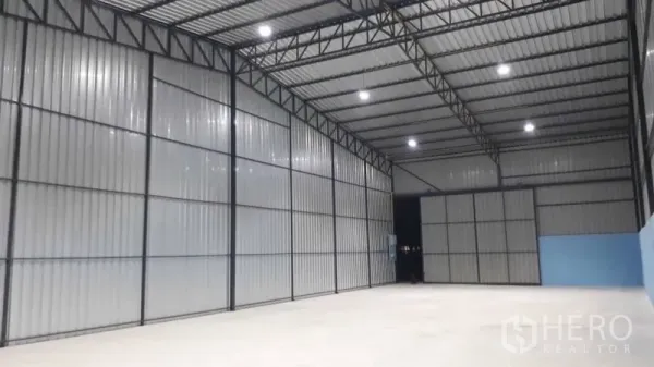 Warehouse for rent in Pak Kret, Nonthaburi - Spacious warehouse interior featuring high steel trusses, bright LED lights, and a smooth concrete floor.