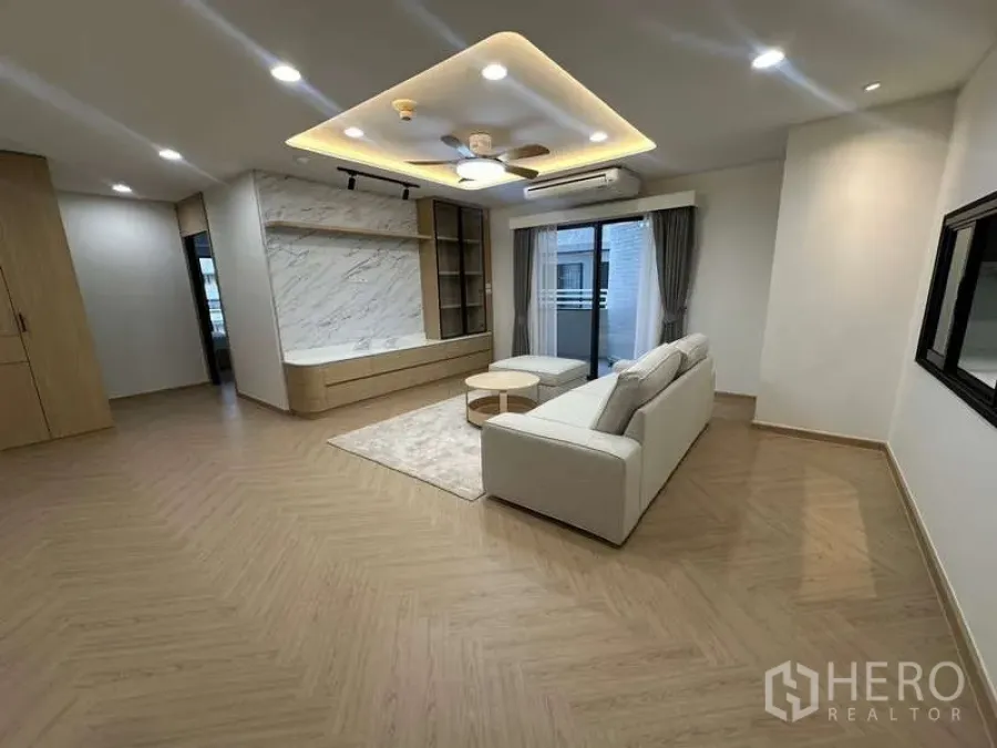 Condominium for rent in Watthana, Bangkok - Living room with L-shaped sofa, marble feature wall and recessed ceiling lighting.