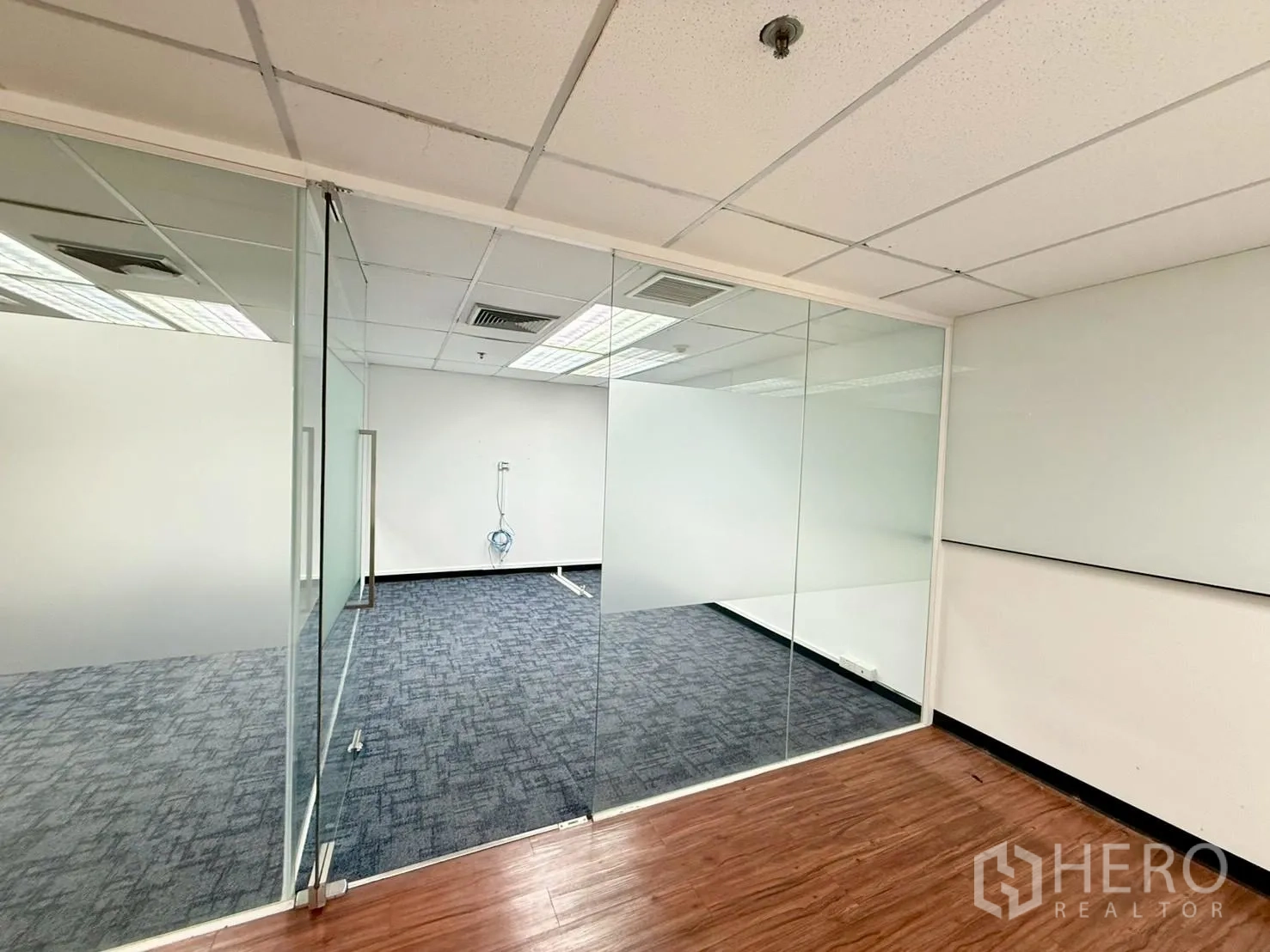 Office Space for rent in Watthana, Bangkok - Glass-walled meeting room with frosted panels and carpet next to wood-look flooring.
