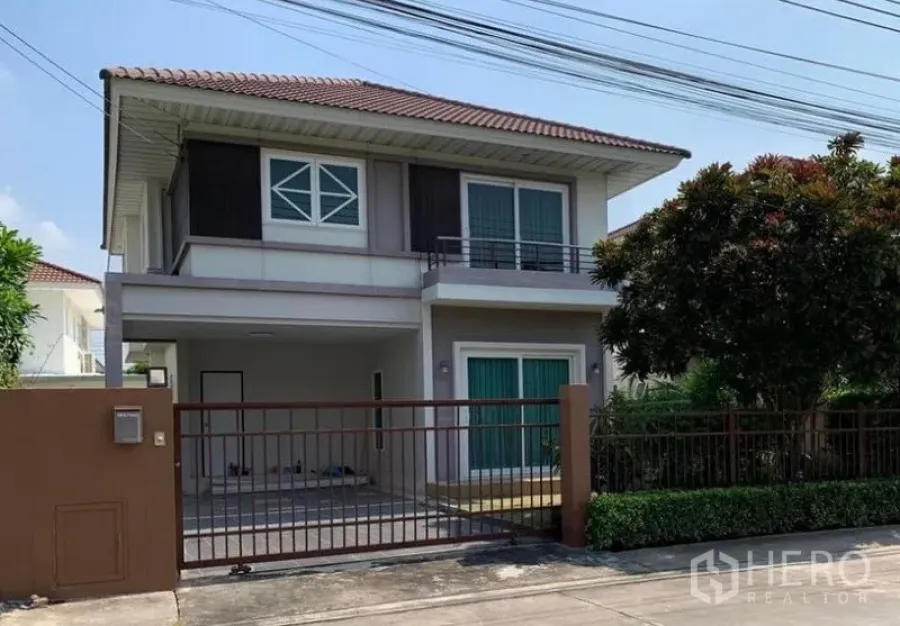 独立式住宅 出售在Bang Phli, Samut Prakan - 两层独栋别墅外观，带入户庭院、可停两车的门控车位与绿篱。