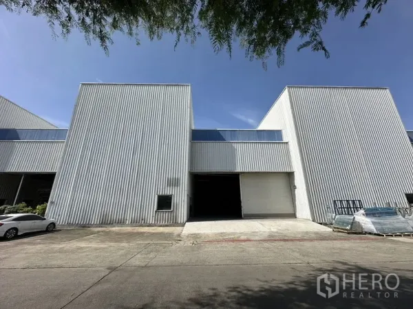 Factory for rent in Khlong Luang, Pathum Thani - Front elevation of corrugated metal factory with large roll-up door and parking apron.