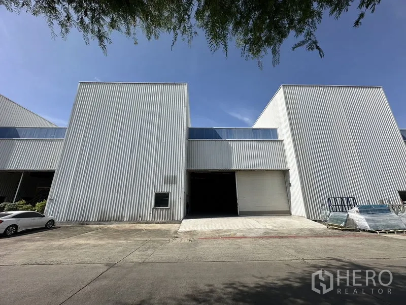 Factory for rent in Khlong Luang, Pathum Thani - Front elevation of corrugated metal factory with large roll-up door and parking apron.