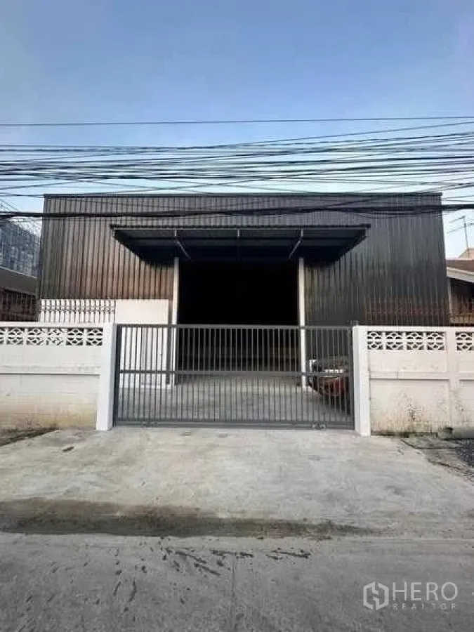 Warehouse for rent in Bang Khen, Bangkok - Street-facing warehouse facade with double awnings, secure sliding gate and concrete apron.