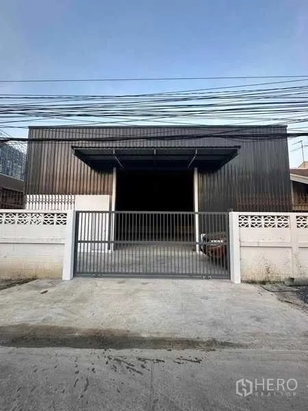Warehouse for rent in Bang Khen, Bangkok - Street-facing warehouse facade with double awnings, secure sliding gate and concrete apron.