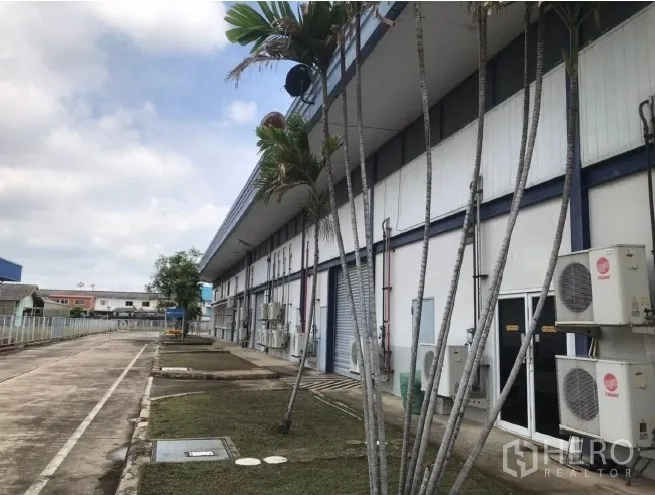Factory for rent in Bang Bua Thong, Nonthaburi - Side of factory with palm trees, AC units and service walkway.