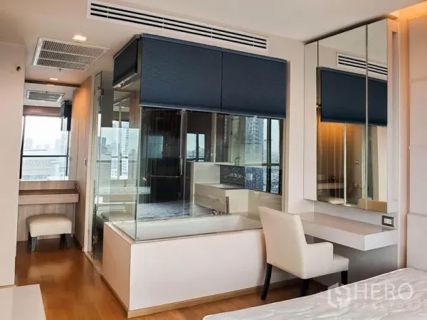 Condominium for rent in Bang Rak, Bangkok - Glass-walled ensuite bathroom with bathtub, large mirrors, and a vanity desk adjoining the bedroom.