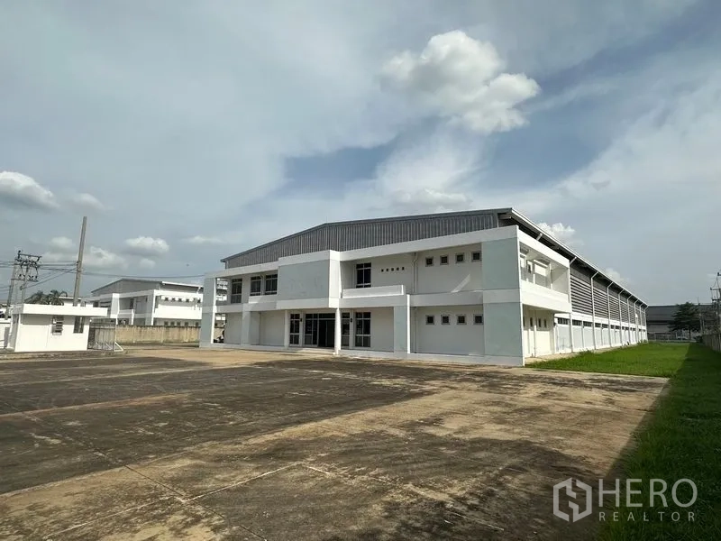 Factory for rent in Phra Nakhon Si Ayutthaya - Modern white factory with metal roof and large paved loading yard under a bright sky in Bang Pa-in.