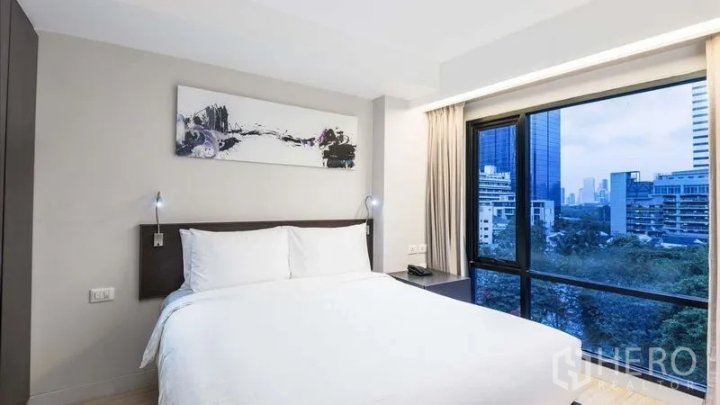 房间 出租在Watthana, Bangkok - 次卧转角窗眺望绿意与城市建筑。