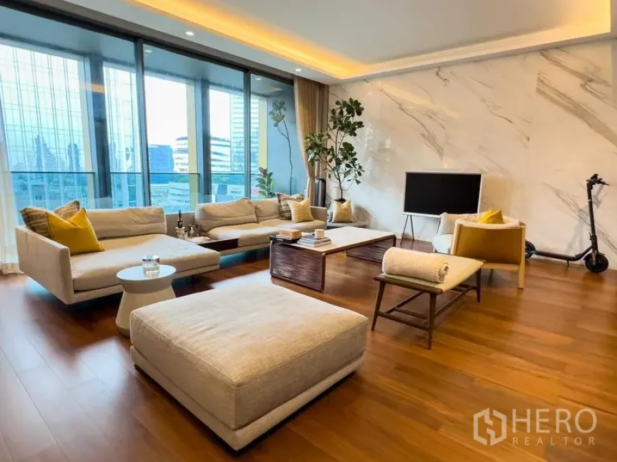 Condominium for sale in Khlong Toei, Bangkok - Another view of the living room showing balcony glazing, sofas and city backdrop.