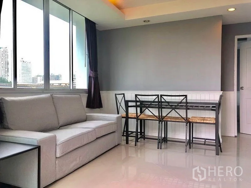 Condominium for rent in Khlong Toei, Bangkok - Living and dining area with sofa, glass table and wide windows overlooking the city.