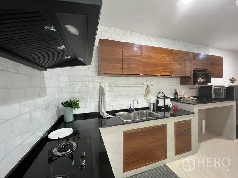 Townhouse for rent - Close-up of fitted kitchen featuring gas hob, extractor hood, stone countertop and wood cabinets.