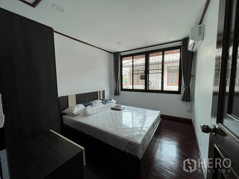 Townhouse for rent in Din Daeng, Bangkok - Second bedroom with large window, security grilles, air conditioner and wood flooring.