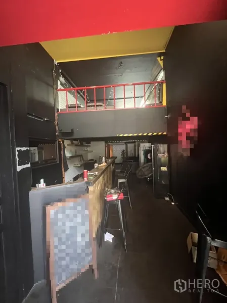 Shophouse for rent in Khlong Toei, Bangkok - Ground‑floor interior featuring a long bar counter with stools and a mezzanine under a dark industrial ceiling.