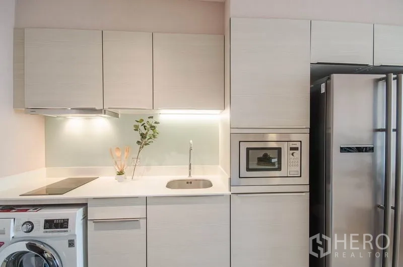 Condominium for rent or sale in Watthana, Bangkok - Compact modern kitchen with built-in cabinets, hob, microwave, fridge and washer.