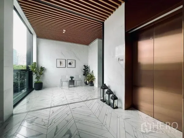 Condominium for sale in Pathum Wan, Bangkok - Elegant private lift lobby with marble floors, wood slat ceiling, bronze elevator doors and potted plants.