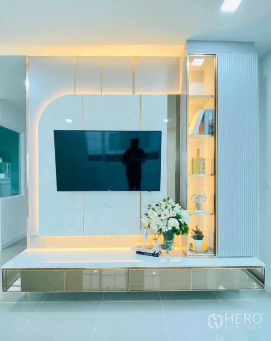 Detached House for rent in Prawet, Bangkok - Modern living room with built-in TV wall, warm LED backlighting and glass display shelving.