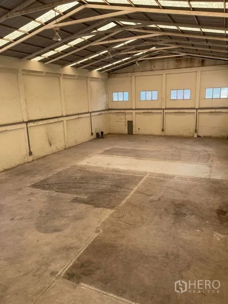 Warehouse for rent in Samut Sakhon - Wide-span warehouse interior showing steel truss roof, suspended lights and clear floor area.