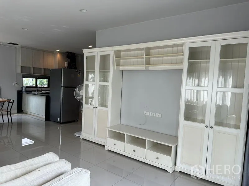 Detached House for rent in Lam Luk Ka, Pathum Thani - Open-plan living area with built-in white display cabinet and view to kitchen.
