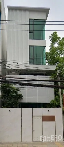 Home Office for rent in Suan Luang, Bangkok - Four-story modern home office facade with large green-tinted windows and a white perimeter wall in Suan Luang.