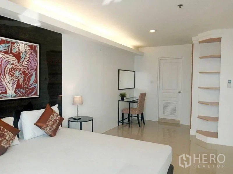 Condominium for rent in Khlong Toei, Bangkok - Spacious master bedroom showing bed, curved corner shelves and door with warm cove lighting.